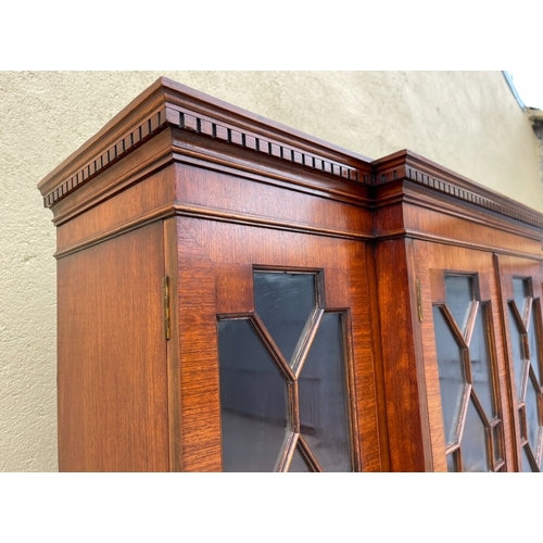 136 - A NEAT SIZED MAHOGANY BREAKFRONT BOOKCASE, with dentil cornice above four astral glazed doors reveal... 