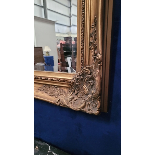 189 - A GOOD QUALITY GILT WALL MIRROR, with raised relief decoration to the frame, and a good bevelled gla... 