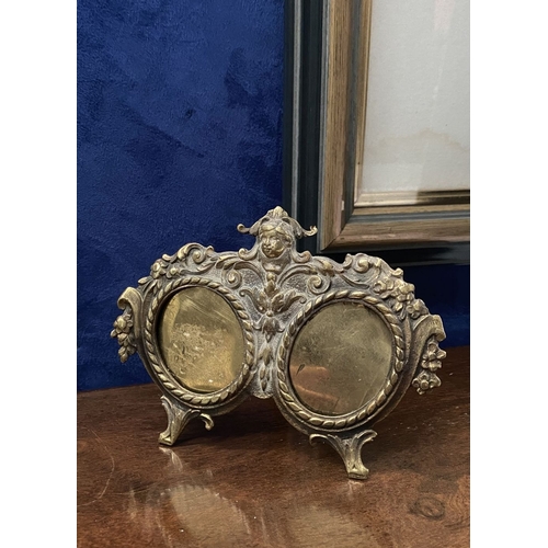 78 - A LATE 19TH CENTURY ORNATE BRASS DOUBLE PHOTO FRAME, the two oval framed with top border, figural mo... 