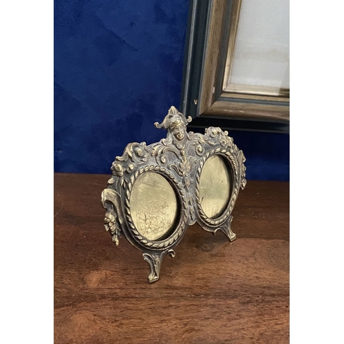 78 - A LATE 19TH CENTURY ORNATE BRASS DOUBLE PHOTO FRAME, the two oval framed with top border, figural mo... 