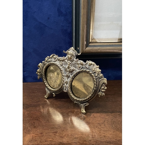 78 - A LATE 19TH CENTURY ORNATE BRASS DOUBLE PHOTO FRAME, the two oval framed with top border, figural mo... 