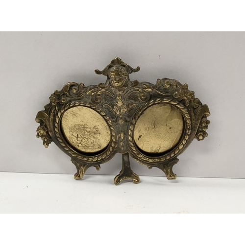 78 - A LATE 19TH CENTURY ORNATE BRASS DOUBLE PHOTO FRAME, the two oval framed with top border, figural mo... 