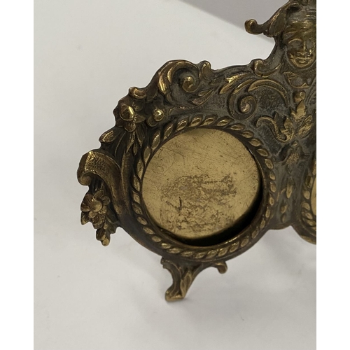 78 - A LATE 19TH CENTURY ORNATE BRASS DOUBLE PHOTO FRAME, the two oval framed with top border, figural mo... 