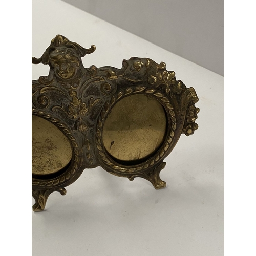 78 - A LATE 19TH CENTURY ORNATE BRASS DOUBLE PHOTO FRAME, the two oval framed with top border, figural mo... 