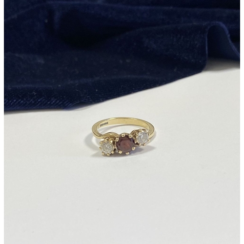 320 - A 9CT YELLOW GOLD GARNET THREE STONE RING, with round cut central garnet in raised claw setting, fla... 