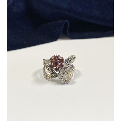 322 - A PRETTY STERLING SILVER GARNET FLORAL CROSSOVER RING, with seven round cut garnets set in floral se... 