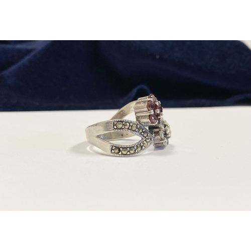 322 - A PRETTY STERLING SILVER GARNET FLORAL CROSSOVER RING, with seven round cut garnets set in floral se... 