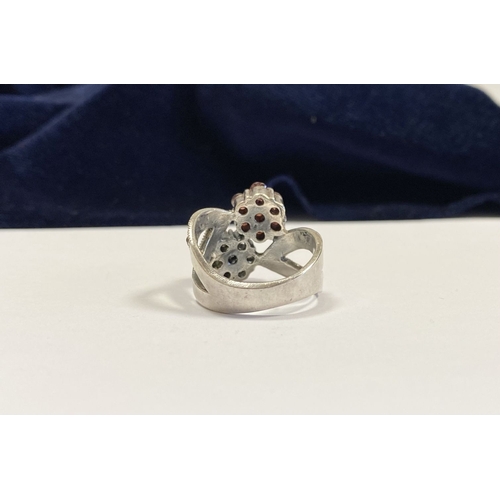 322 - A PRETTY STERLING SILVER GARNET FLORAL CROSSOVER RING, with seven round cut garnets set in floral se... 