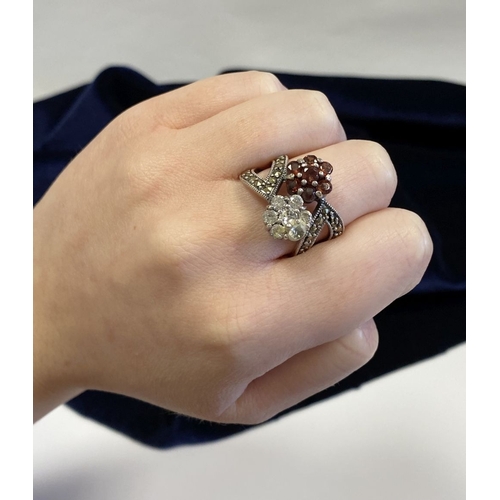 322 - A PRETTY STERLING SILVER GARNET FLORAL CROSSOVER RING, with seven round cut garnets set in floral se... 