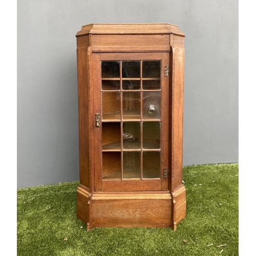 229 - AN ANTIQUE OAK CORNER DISPLAY CABINET, with glazed door revealing shelved interior above shaped base... 