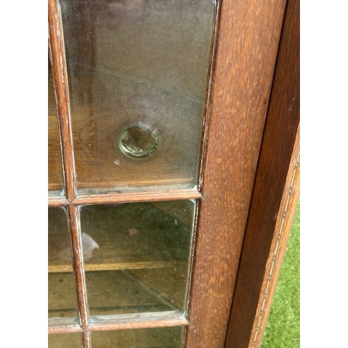 229 - AN ANTIQUE OAK CORNER DISPLAY CABINET, with glazed door revealing shelved interior above shaped base... 