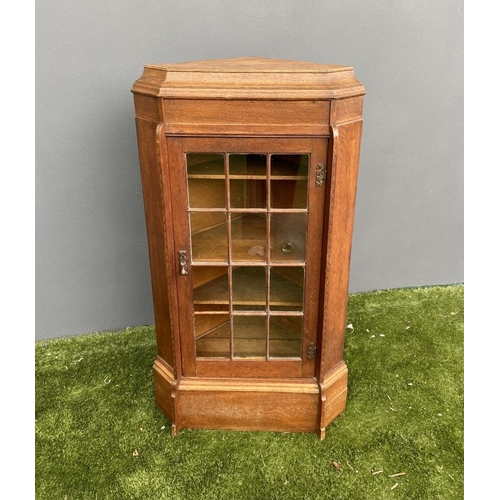 229 - AN ANTIQUE OAK CORNER DISPLAY CABINET, with glazed door revealing shelved interior above shaped base... 