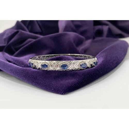 82 - AN 18CT WHITE GOLD-PLATED SAPPHIRE BANGLE BRACELET, featuring five oval cut sapphires, claw set, sur... 