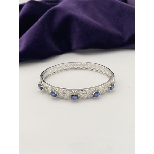 82 - AN 18CT WHITE GOLD-PLATED SAPPHIRE BANGLE BRACELET, featuring five oval cut sapphires, claw set, sur... 