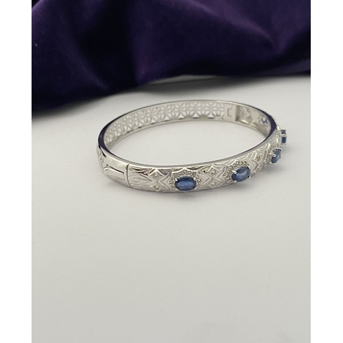 82 - AN 18CT WHITE GOLD-PLATED SAPPHIRE BANGLE BRACELET, featuring five oval cut sapphires, claw set, sur... 