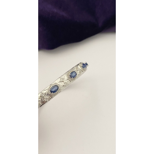 82 - AN 18CT WHITE GOLD-PLATED SAPPHIRE BANGLE BRACELET, featuring five oval cut sapphires, claw set, sur... 