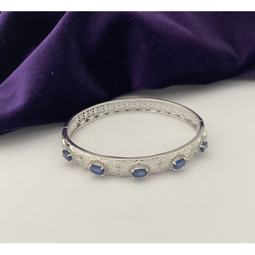 82 - AN 18CT WHITE GOLD-PLATED SAPPHIRE BANGLE BRACELET, featuring five oval cut sapphires, claw set, sur... 