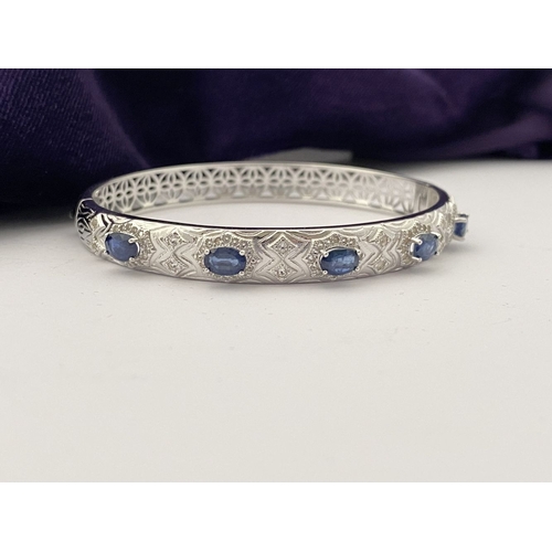 82 - AN 18CT WHITE GOLD-PLATED SAPPHIRE BANGLE BRACELET, featuring five oval cut sapphires, claw set, sur... 