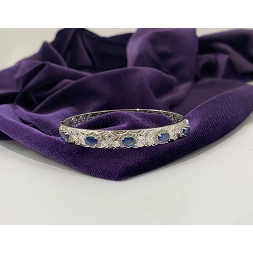82 - AN 18CT WHITE GOLD-PLATED SAPPHIRE BANGLE BRACELET, featuring five oval cut sapphires, claw set, sur... 