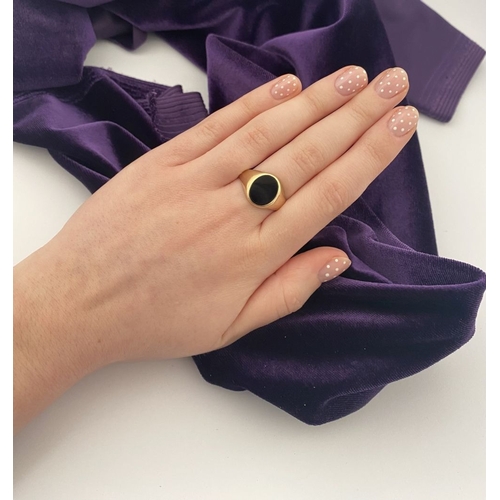 83 - AN IRISH 9CT GOLD GENTLEMAN'S ONYX SIGNET RING, featuring oval onyx in bezel setting, with tapered s... 