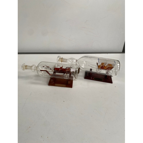 355 - 2x glass old car & glass horse carriage in bottles on plinths