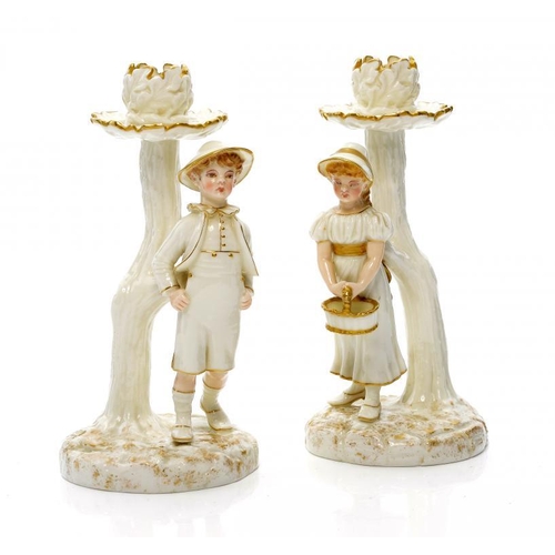 224 - A PAIR OF ROYAL WORCESTER GLAZED PARIAN WARE BOY AND GIRL CANDLESTICKS MODELLED BY JAMES HADLEY IN T... 