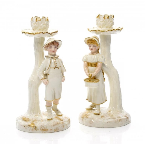 225 - A PAIR OF ROYAL WORCESTER GLAZED PARIAN WARE BOY AND GIRL CANDLESTICKS MODELLED BY JAMES HADLEY IN T... 