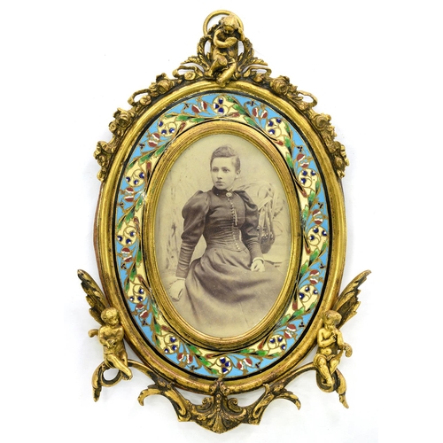 274 - A FRENCH OVAL ORMOLU AND CHAMPLEVE ENAMEL PHOTOGRAPH FRAME, APPLIED WITH PUTTI, 26CM H, C1880