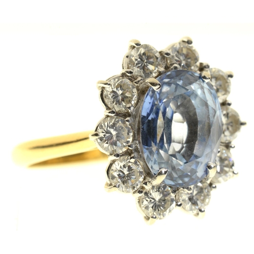 9 - A CORNFLOWER SAPPHIRE AND DIAMOND RING  the oval sapphire in a surround of ten evenly sized round br... 