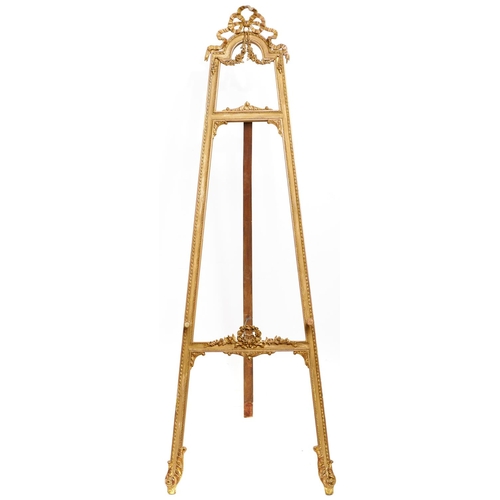 1603 - A French giltwood and composition salon easel, early 20th c, in Louis XVI style, crested by a bow an... 