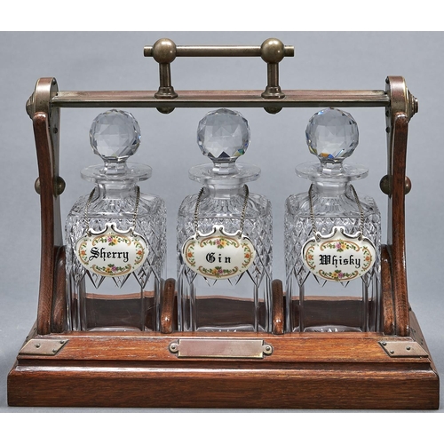 1085 - An Edwardian oxidised brass mounted oak tantalus, Grinsell's Patent, containing three cut glass deca... 