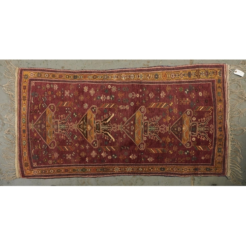 1446 - A Caucasian multi coloured bordered rug, the brown ground worked with four stylise floral filled urn... 