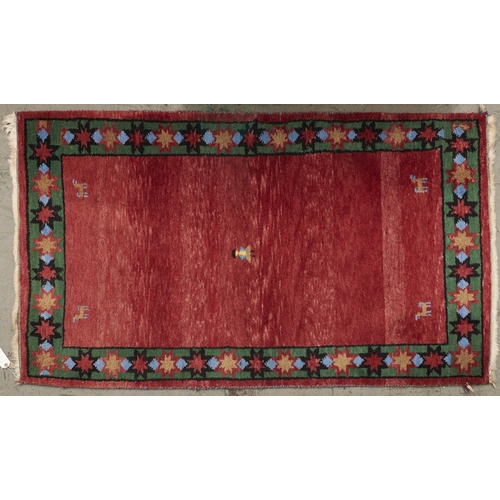 1447 - A modern woollen rug, the red ground worked with central stylised figure and animals to the spandrel... 