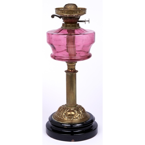 519 - An Edwardian brass oil lamp, with cranberry glass fount and brass burner, on black glazed foot, 45cm... 