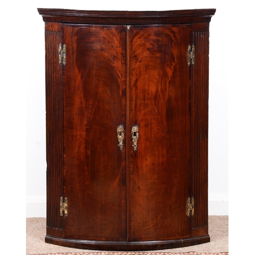 982 - A George III mahogany hanging corner cupboard, the cavetto cornice above figured doors with brass es... 