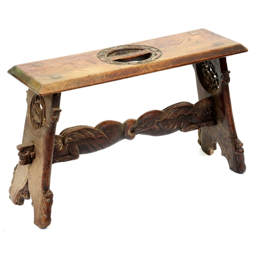 519 - A Victorian medievalist trestle stool, carved and pierced to the top with a central ring of grotesqu... 