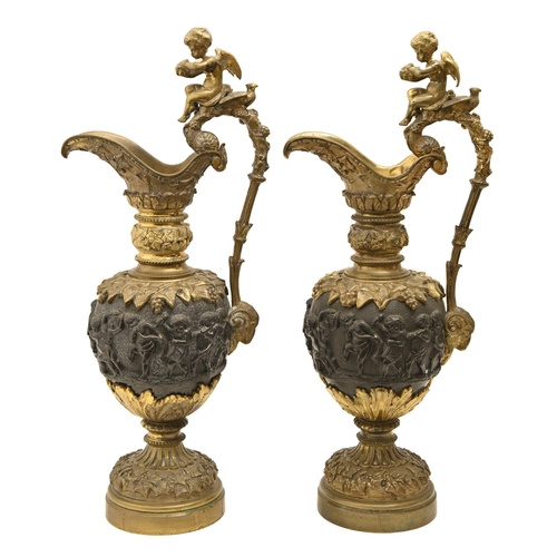 928 - A pair of patinated bronze ornamental ewers, late 19th c, cast with bacchanalian revelry, the scroll... 