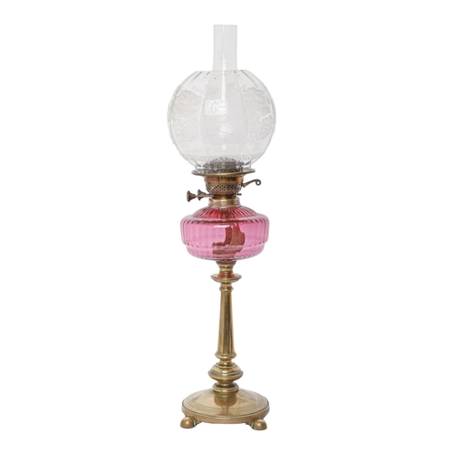 218 - A brass oil lamp, c1900, on round base and four ball feet, moulded cranberry glass fount, brass burn... 