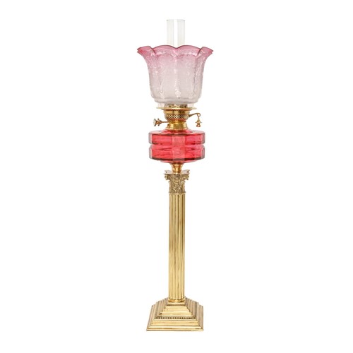 210 - A brass Corinthian column oil lamp, c1900, with faceted cranberry glass fount and brass duplex burne... 