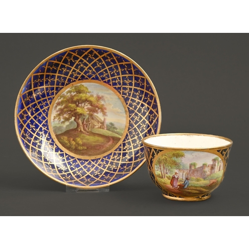 569 - A Derby teacup and saucer, c1815, painted with landscapes reserved on a cobalt and gilt trellis grou... 