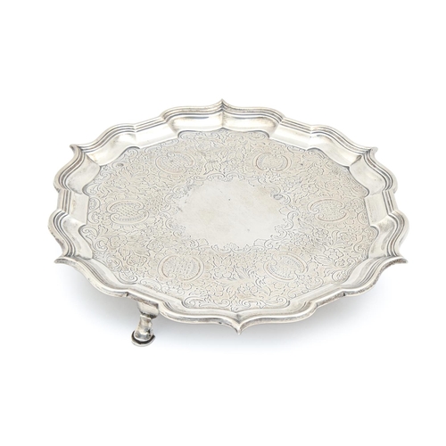 520 - A Victorian silver salver, the field engraved with flowers and C-scrolls within bath border, on thre... 