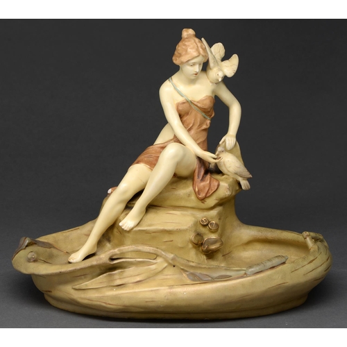 691 - A Royal Dux figural dish, early 20th c, in the form of a maiden with doves on the bank of a lily poo... 