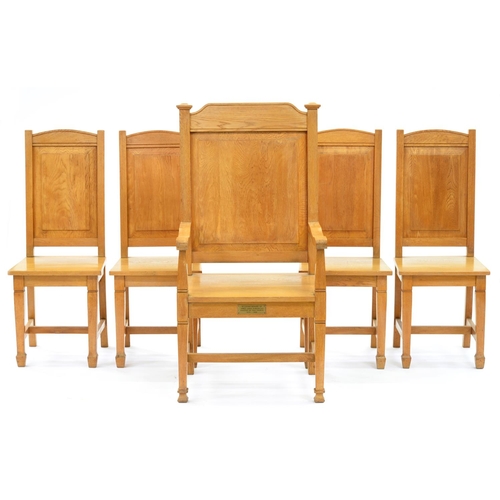 1219 - A set of five light oak panel back chairs, mid 20th c, including an armchair with brass memorial tab... 