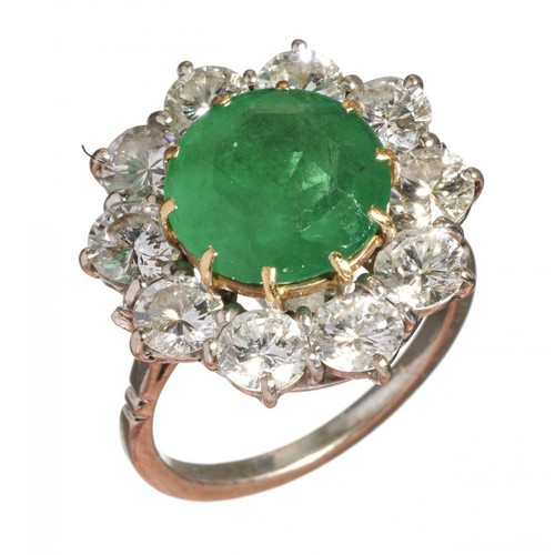 24 - An emerald and diamond ring, the emerald 11mm diam, head 20mm diam, in a surround of ten round brill... 