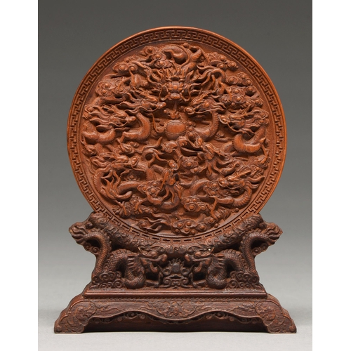 206 - A Chinese sandalwood roundel, 19th c, finely carved with dragons in key fret border, on carved wood ... 