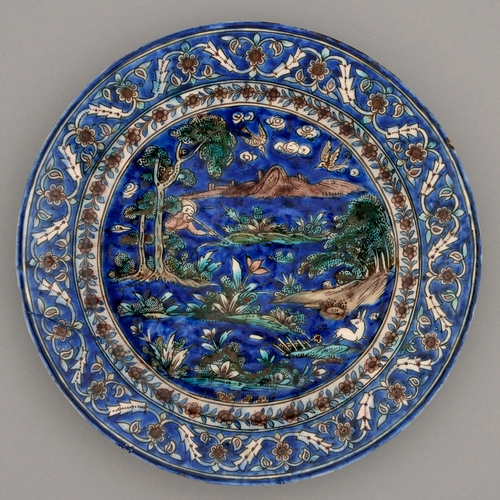 479 - A Persian frit paste dish, Qajar dynasty, 19th c, painted with a hunter, deer and birds amidst veget... 