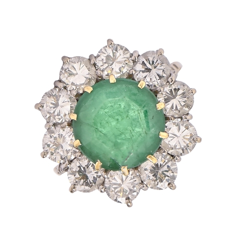 24 - An emerald and diamond ring, the emerald 11mm diam, head 20mm diam, in a surround of ten round brill... 