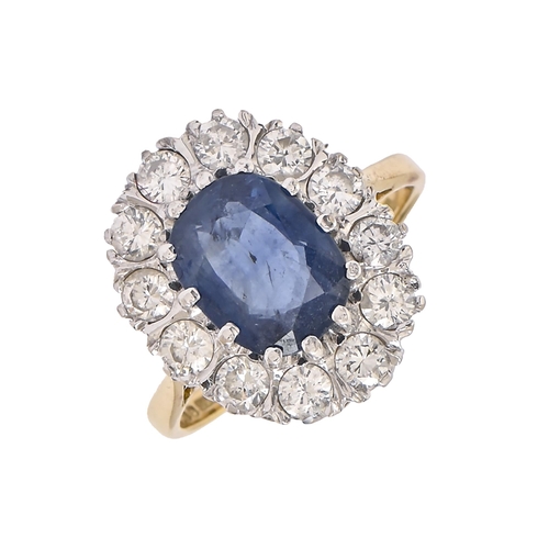53 - A sapphire and diamond ring, the larger central oval sapphire in a surround of twelve diamonds, in 1... 