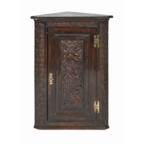 864 - A Victorian carved and stained oak hanging corner cupboard, the door with putti and brass 'H'-hinges... 