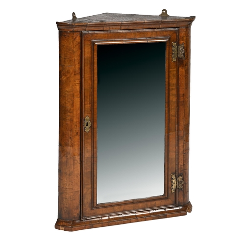 877 - A walnut hanging corner cupboard, late 19th c, the door with bevelled mirror in cushion moulding and... 